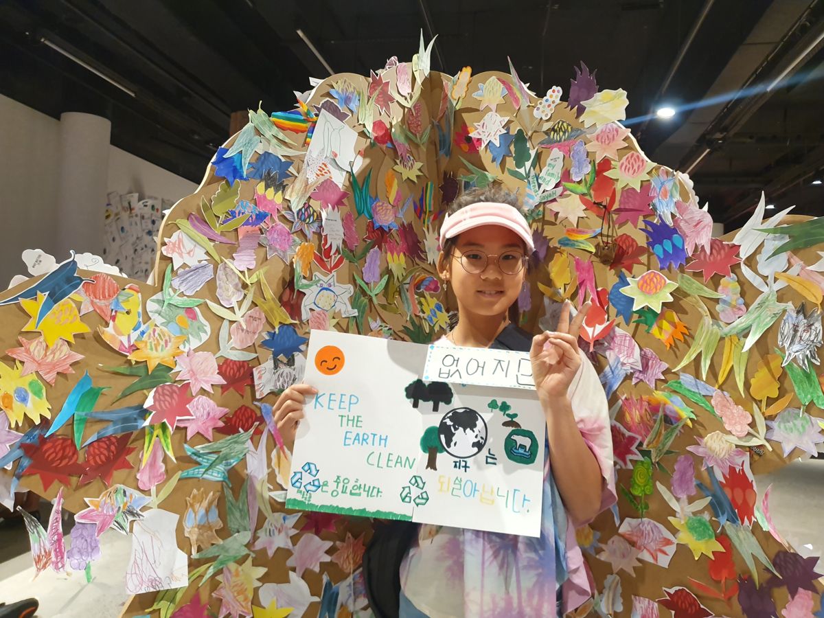 Holding a handmade sign in front of a wall of paper cranes